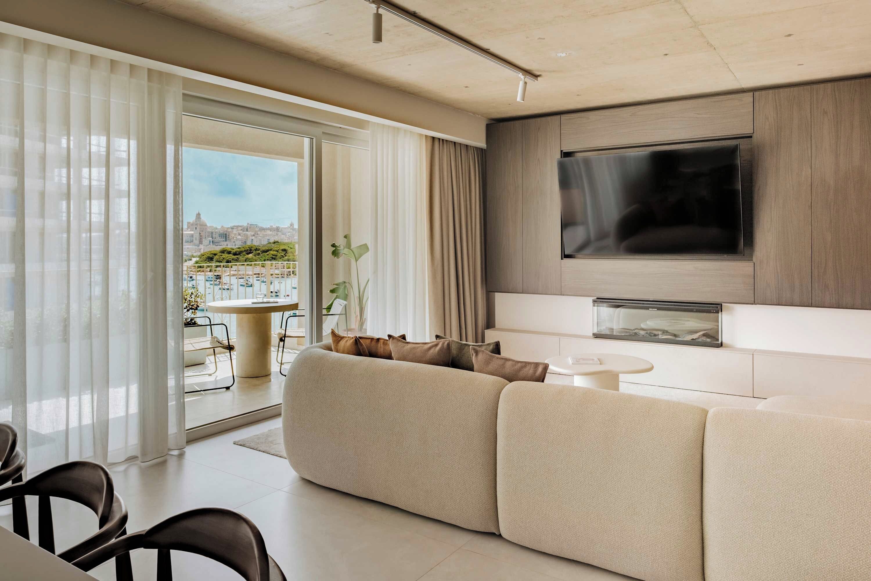 Un salon moderne avec un grand canapé, un téléviseur à écran plat fixé au mur et un coin repas comprenant une table et des chaises.