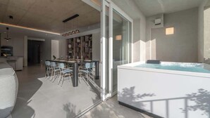 Un interior moderno con zona de comedor, bañera de hidromasaje y cocina visible a través de puertas de cristal.