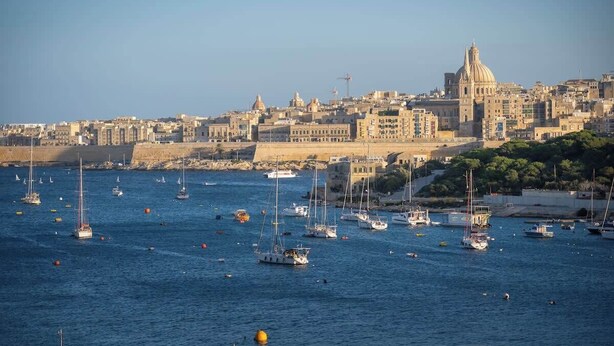 Un paisaje urbano costero con un edificio histórico destacado y un puerto deportivo lleno de barcos.