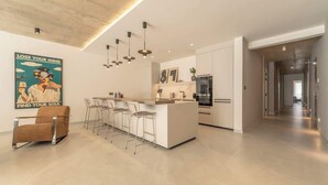 Una cocina moderna con una isla central, taburetes de bar, iluminación colgante y un póster en la pared.