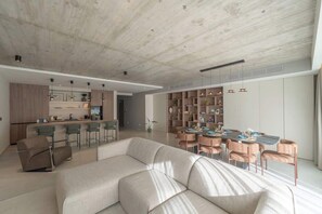 Ein modernes Wohnzimmer mit einer Couch, einem Esstisch mit Stühlen und einer Küchenzeile mit Barhocker.