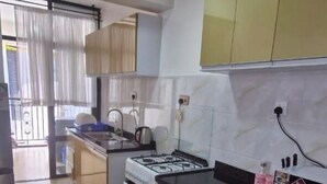 A kitchen with a gas stove, oven, and a sink. There is a window with curtains, and a door leading to another room. - Cobot Suites Marcus Garden (Nairobi)