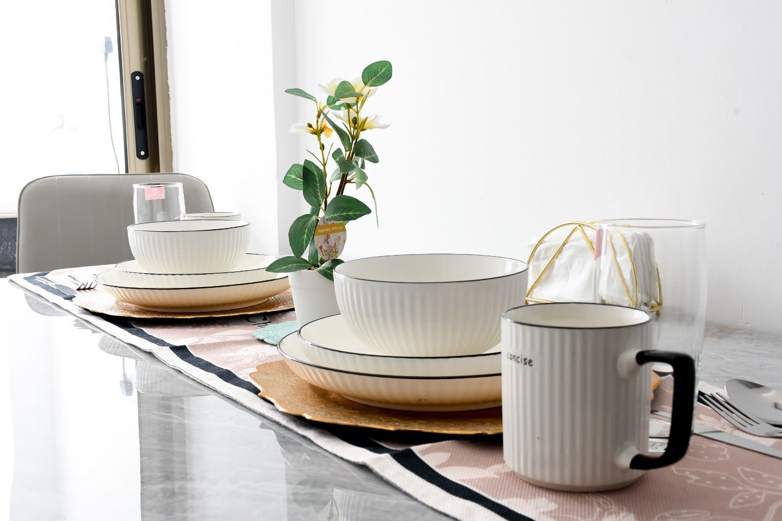 A dining table set with white plates, bowls, and a mug, accompanied by a plant and a tissue.