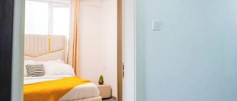 A bedroom with a bed, a small bedside table, and a window with curtains.