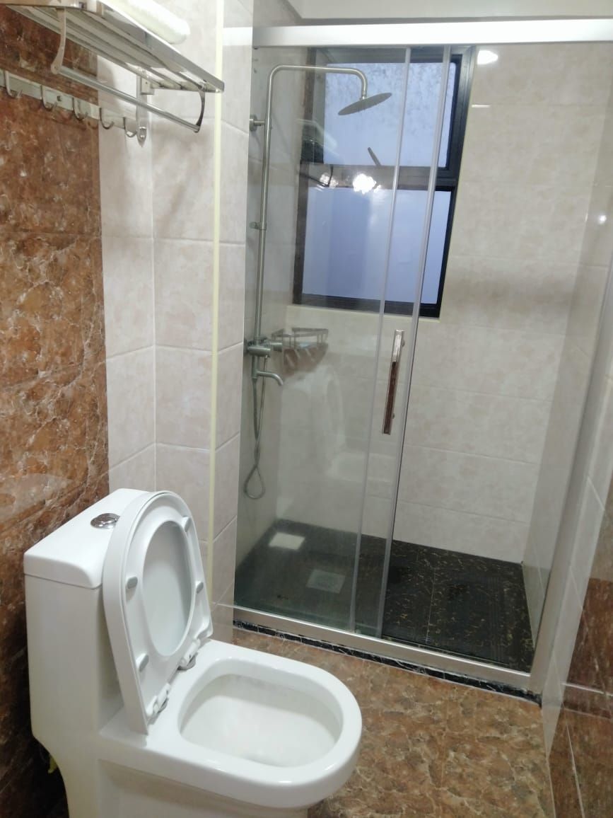A bathroom with a glass-enclosed shower, a toilet, and a marble-tiled floor.