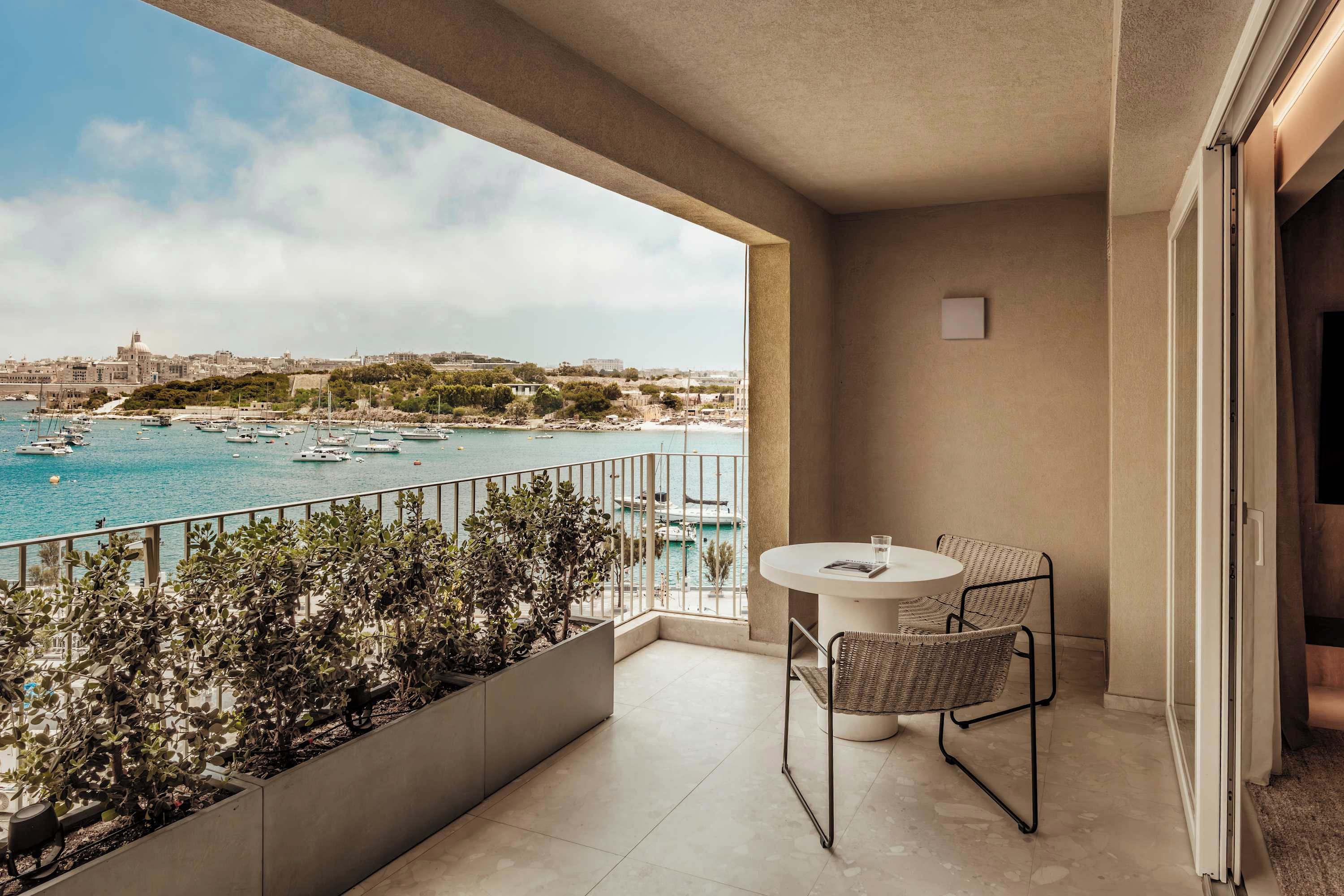 A balcony with a table and chairs, overlooking a marina with boats and a cityscape.