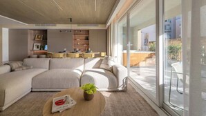 Ein modernes Wohnzimmer mit einer Eckcouch, einem Couchtisch mit Pflanze und einem durch eine Glastür einsehbaren Küchenbereich.