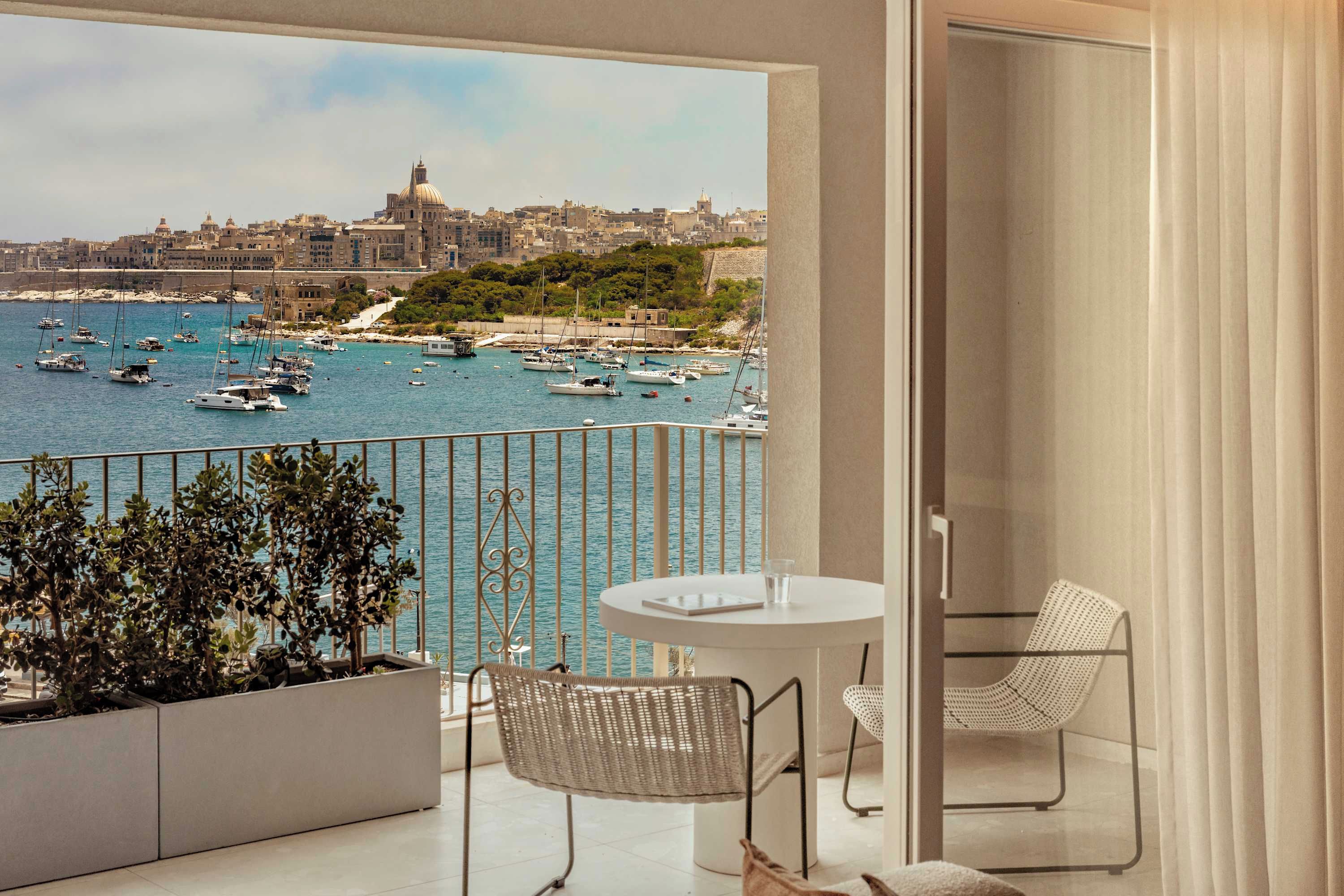Un balcon donnant sur un port, une table, deux chaises et des plantes en pot.