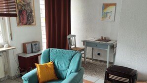 A living room with a teal armchair, a wooden coffee table, a black radio, a white chair, and a painting on the wall. - Apartment 'Ferienunterkunft Göhlich' with Balcony and Wi-Fi (Maintal)