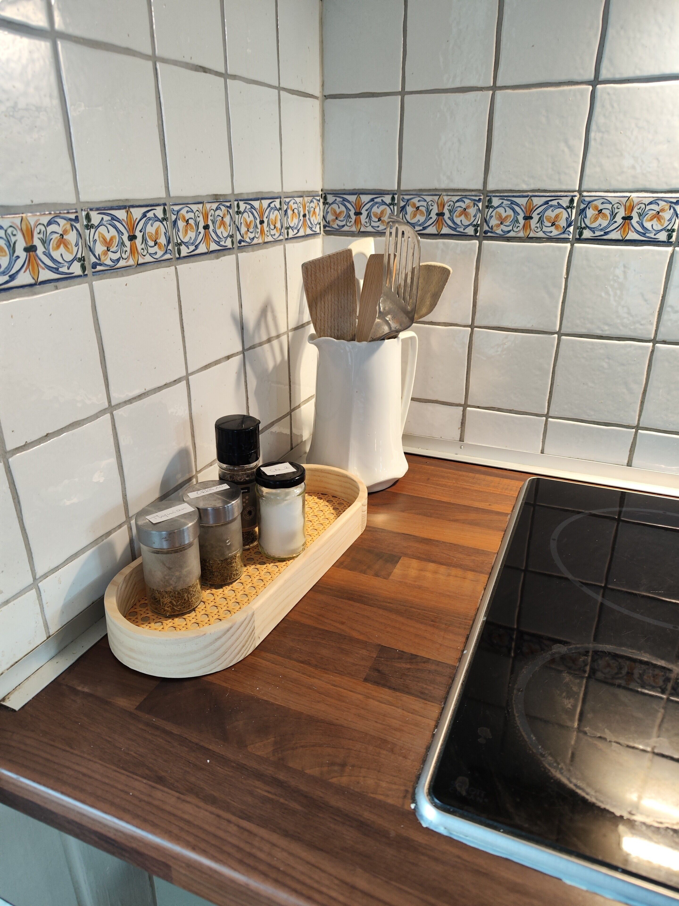 Eine Küche mit weißen Fliesen, einem Holztablett mit Gewürzgläsern und einem weißen Behälter für Holzkocher.