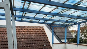 A covered patio area with a round table and two chairs, a tiled floor, and a metal roof structure. - Apartment 'Ferienunterkunft Göhlich' with Balcony and Wi-Fi (Maintal)