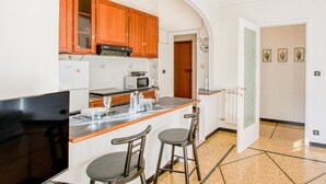 A compact kitchen with wooden cabinets, a microwave, and a small dining area with stools. - Lovely apartment in Rapallo with WiFi (Rapallo)