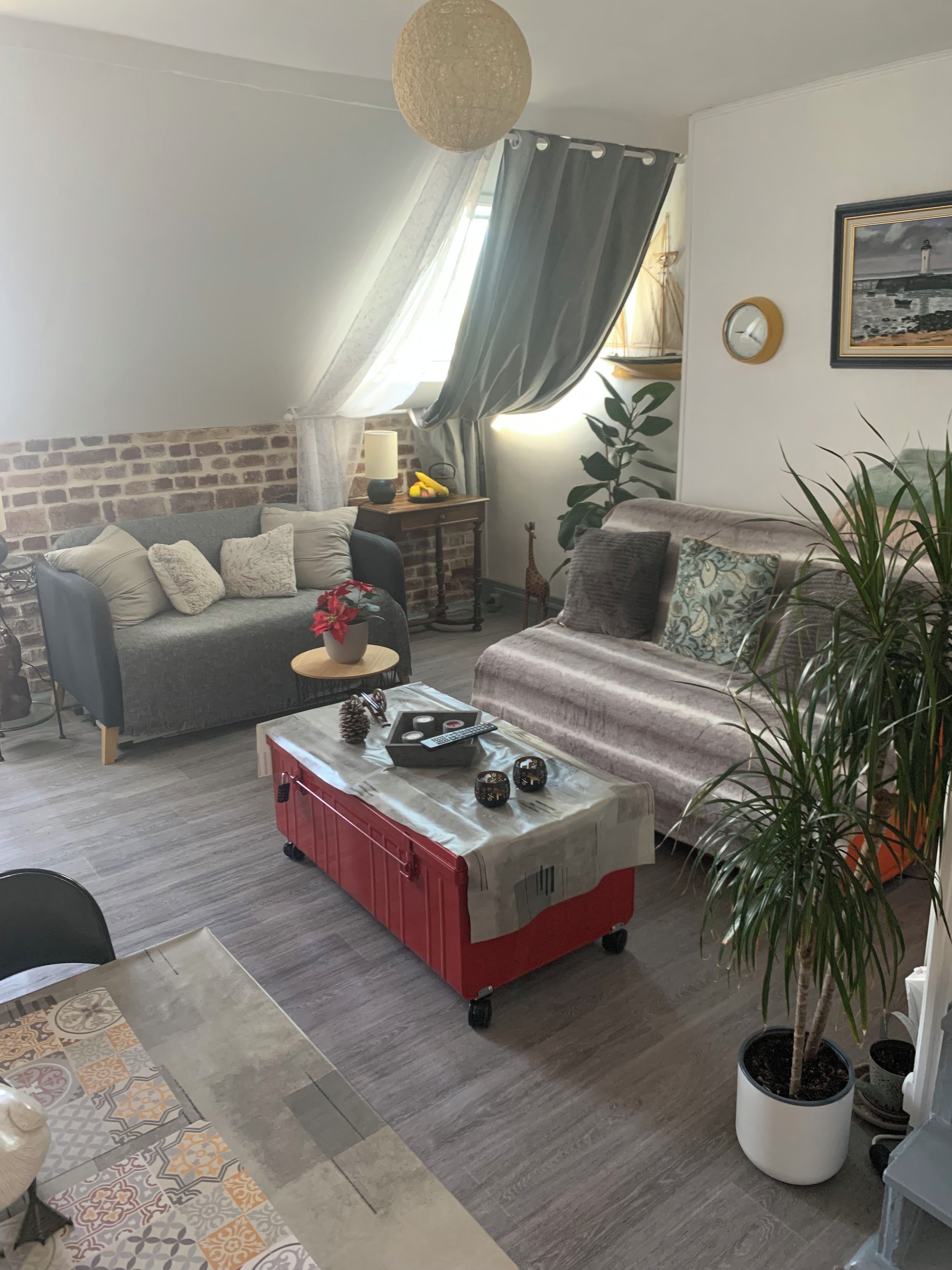 Un salon chaleureux avec un canapé, un meuble de rangement rouge, une plante en pot et une horloge murale.