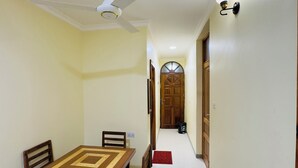 Un comedor con mesa y sillas de madera, un ventilador de techo y un pasillo que conduce a una puerta.