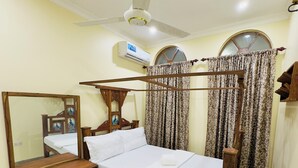 Una cama individual con estructura de madera, una mesita de noche, un espejo y un ventilador de techo.