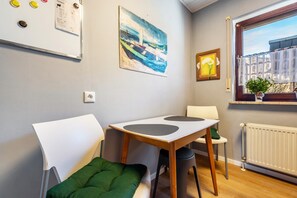 Ein Zimmer mit einem weißen Tisch, zwei Stühlen, einem grünen Kissen, einem Bild, einem Fenster mit Aussicht und einem Heizkörper.