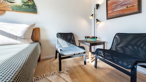 Ein Zimmer mit einem Bett, einem schwarzen Schlafsofa, einem Sessel, einem kleinen Tisch und zwei Wandleuchten.