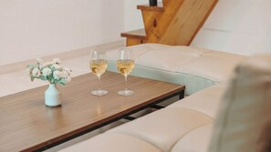 A table with two glasses of white wine, a vase with flowers, and a wooden chair. - Yeosu The Haru Ocean View Pension (Yeosu)