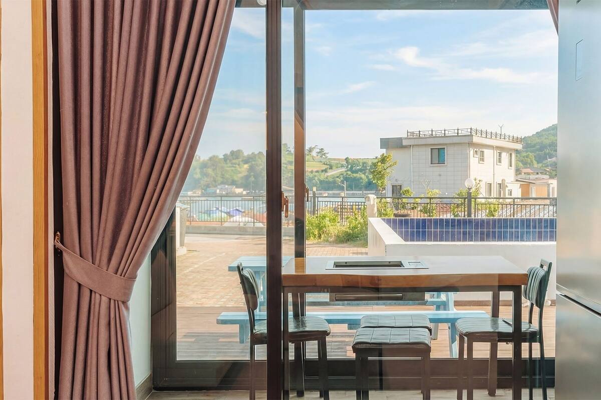 Un balcon avec une table et des chaises, une vue sur un bâtiment situé de l’autre côté d’une étendue d’eau, et un rideau partiellement tiré.