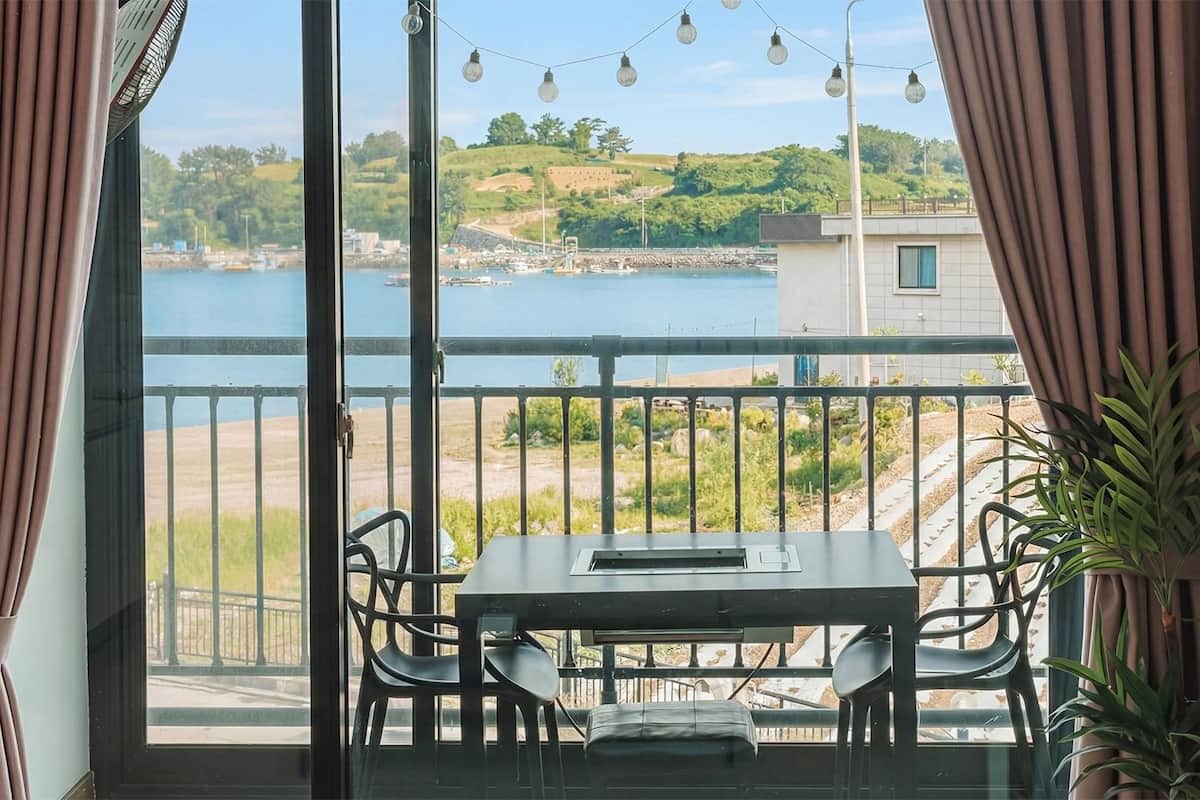 Un balcon avec une table et des chaises, donnant sur une étendue d’eau et sur de la verdure.