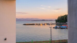 Vista costera con muelle, barcos y montañas al fondo.