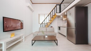 Una sala de estar moderna con televisor de pantalla plana, un sofá, una mesa de centro y una cocina con refrigerador y una escalera.