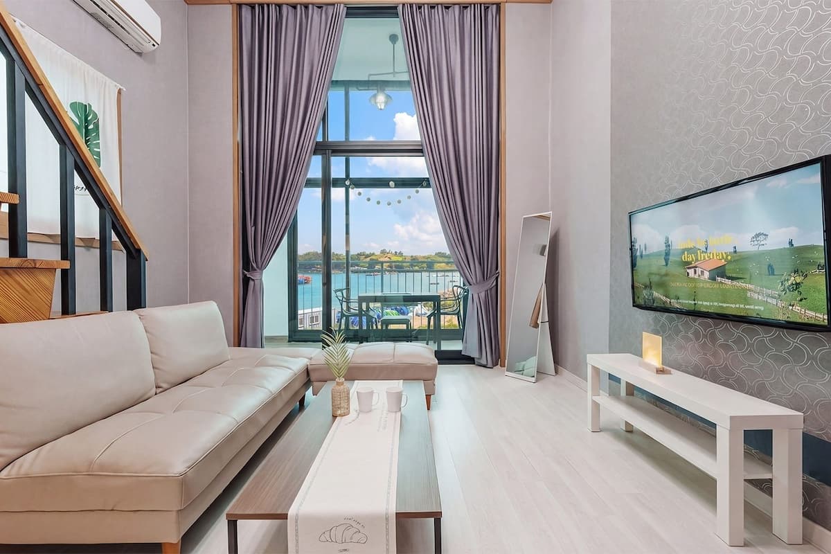 Un salon moderne avec un canapé, une table basse, un téléviseur et un balcon offrant une vue sur la mer.