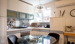 A modern kitchen with stainless steel appliances, a glass dining table, and a window providing natural light. - Jolie Maison (Pesaro)