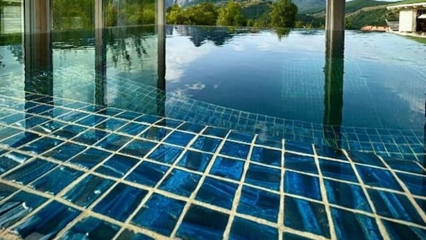 Una piscina infinita en el interior con vistas despejadas a montañas y vegetación a través de amplios ventanales.