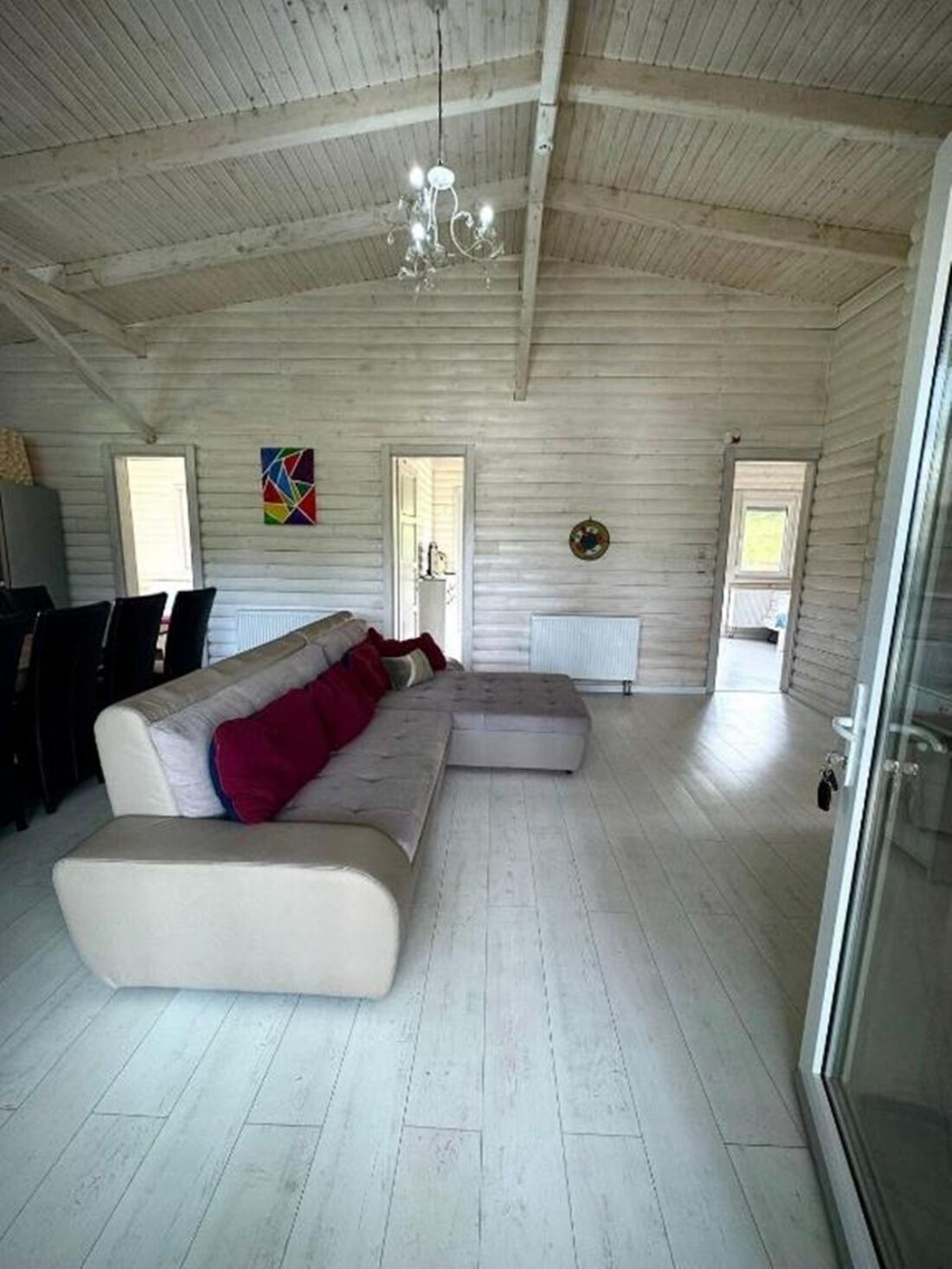 A spacious living room with a large beige sectional sofa, a glass door leading outside, and a wooden ceiling.