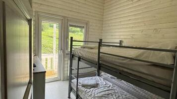 A dormitory room with bunk beds, a desk, and a window.