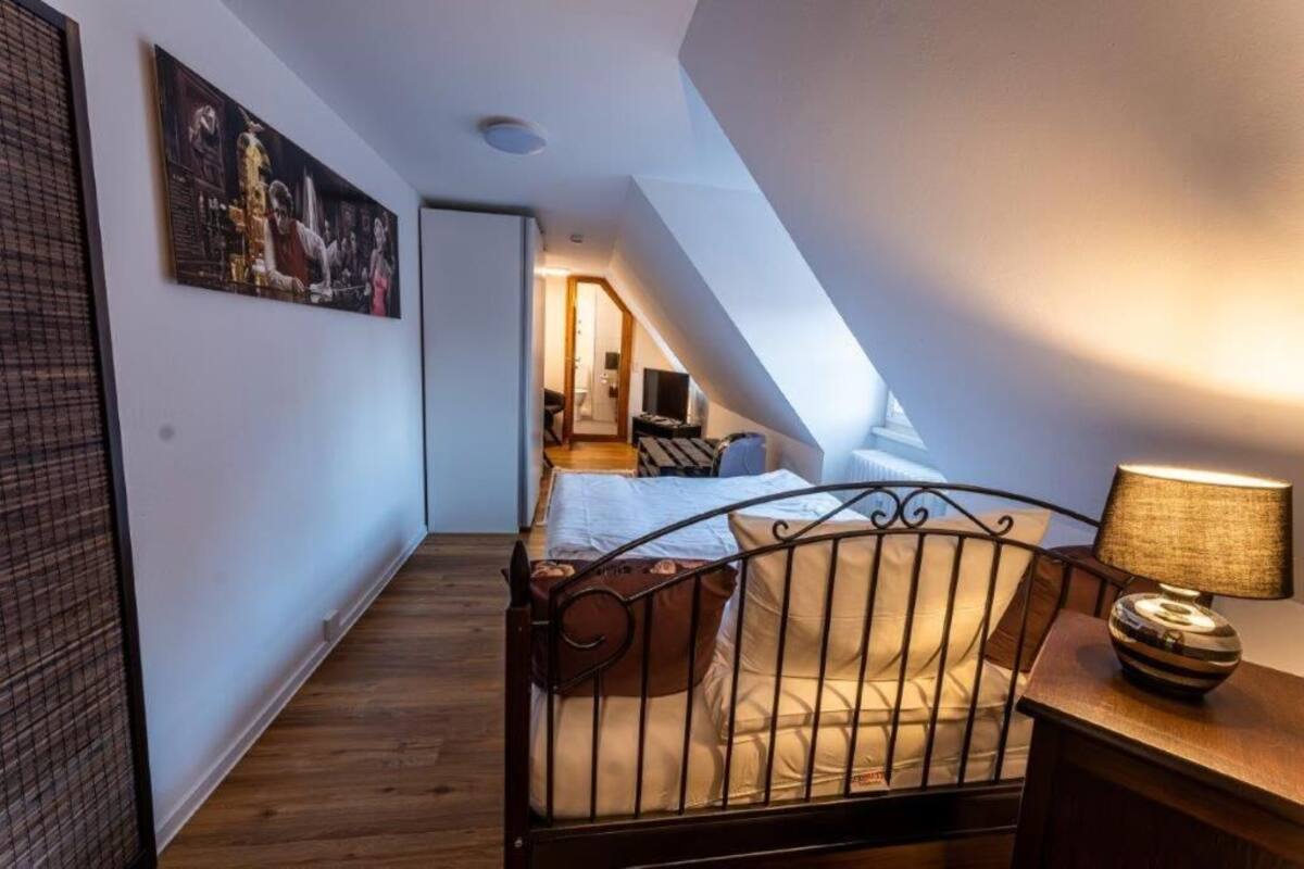 A bedroom with a sloped ceiling, a bed with a headboard, a bedside table with a lamp, and a painting on the wall.