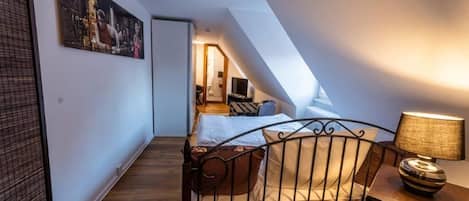 A bedroom with a sloped ceiling, a bed with a headboard, a bedside table with a lamp, and a painting on the wall.