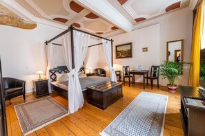 A four-poster bed with a canopy, a wooden desk, a chair, a small table, and a potted plant in a hotel room. - Dicker Mann Hotel Zum Blauen Krebs (Regensburg)