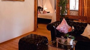 A room with a wooden ceiling, a chandelier, a black leather sofa, a glass coffee table, and a bed with a canopy. - Dicker Mann Hotel Zum Blauen Krebs (Regensburg)