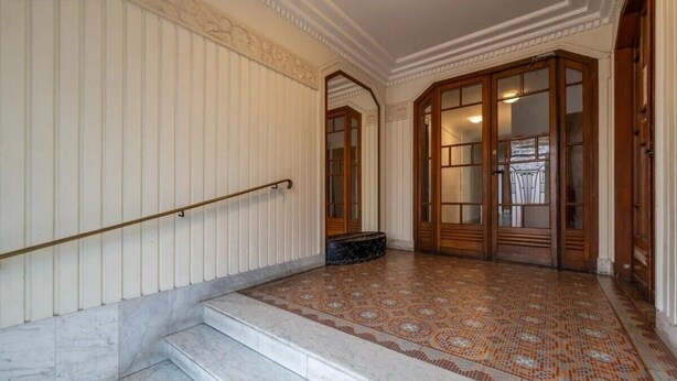 Een statige trap met marmeren treden die leidt naar een kamer met een vloer van patronen en houten deuren.