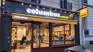Een gevel van Columbus Cafe & Co met een glazen etalage die etenswaren toont, en een toegankelijke ingang voor rolstoelen.