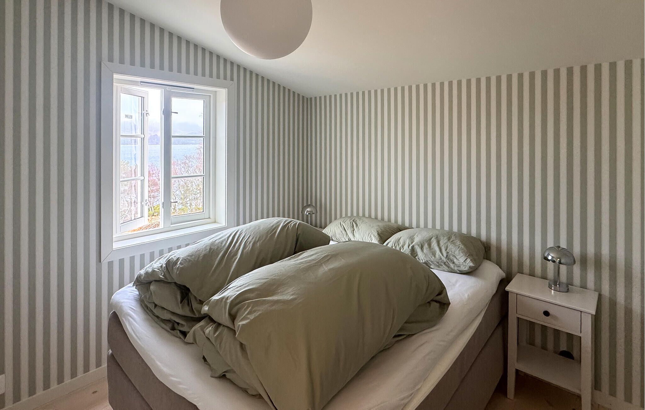 Camera da letto con un letto singolo, un comodino, una lampada e una finestra con vista sugli alberi.
