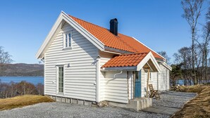 A white house with a red-tiled roof, a chimney, and a view of a lake. - Beach front home in Vikebygd with WiFi (Vikebygd)