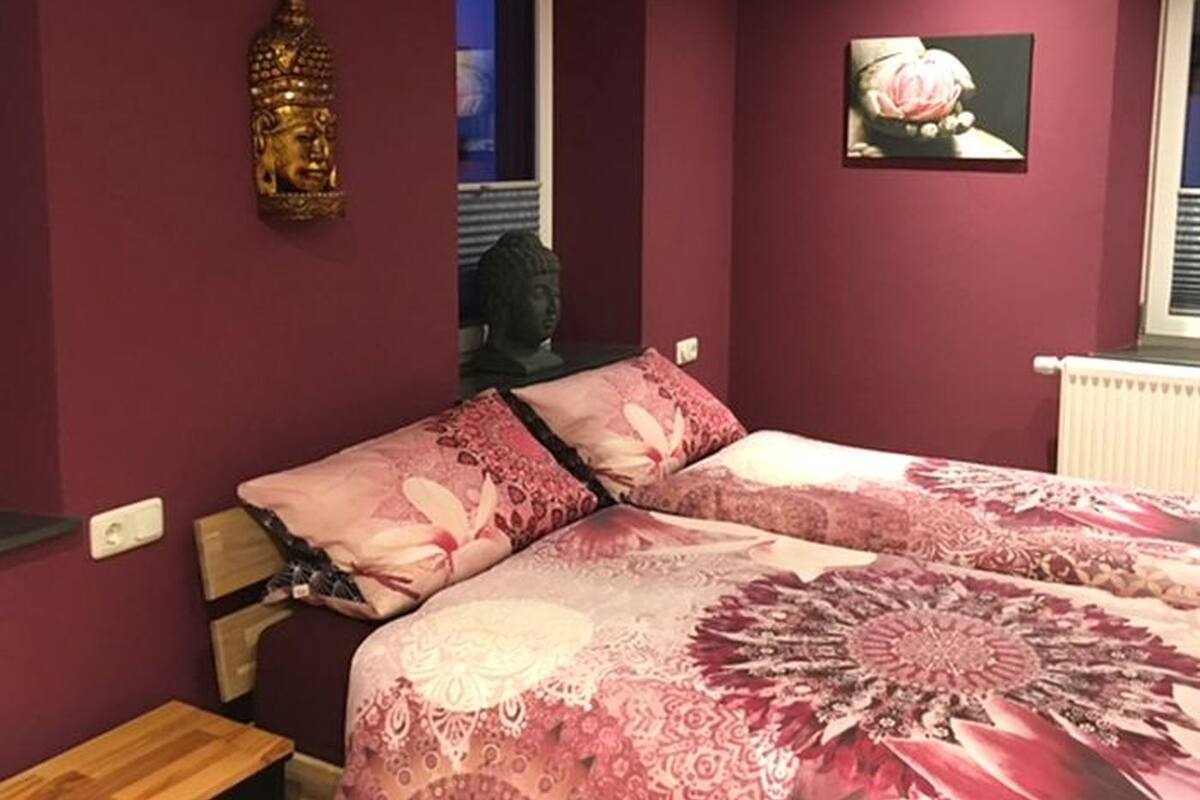 Een slaapkamer met een bed, een raam, een Boeddhabeeld en een roos schilderij.