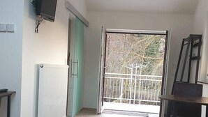 Een kamer met een radiator, een aan de muur bevestigde televisie, een eettafel met stoelen en een balkon met een metalen hekwerk.