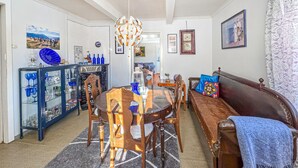 Un comedor con una mesa redonda, sillas y una araña. Hay un sofá con una manta y un cojín decorativo. Un aparador con puertas de cristal exhibe varios objetos.