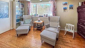Una habitación acogedora con dos sillones de estampado pata de gallo, una mesita de madera, una estantería y una ventana con cortinas.