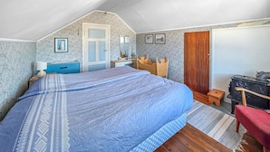 Un dormitorio con una cama grande, un aparador de madera, un taburete pequeño, una silla roja y una estufa.