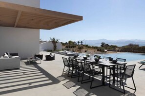 Ein Essbereich im Freien mit Blick auf einen Pool, ausgestattet mit einem Tisch für vier Personen, Stühlen, einer Couch und einem kleinen Tisch mit einer Vase.