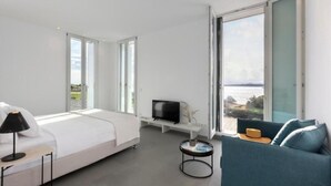 Moderni hotellihuone, jossa on suuri sänky, televisio, sohva ja näkymä merelle.