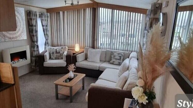Un salon moderne avec une cheminée, un ensemble de canapés, une table basse et une grande fenêtre avec des rideaux.