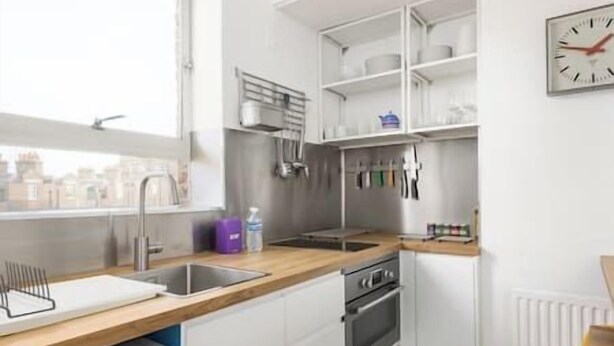 Une cuisine moderne avec des armoires blanches, un plan de travail en bois, un four encastré et une fenêtre donnant sur un paysage urbain.