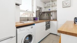 Une cuisine compacte équipée d’un lave-linge, d’un évier et d’un plan de travail en bois.