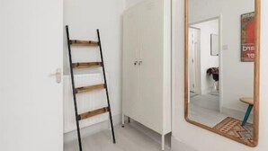 Un couloir avec une armoire blanche, une échelle en bois et un miroir qui reflète une porte et une affiche.